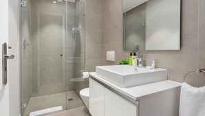 Un baño moderno con ducha envuelta en vidrio, un lavamanos blanco y un espejo grande.