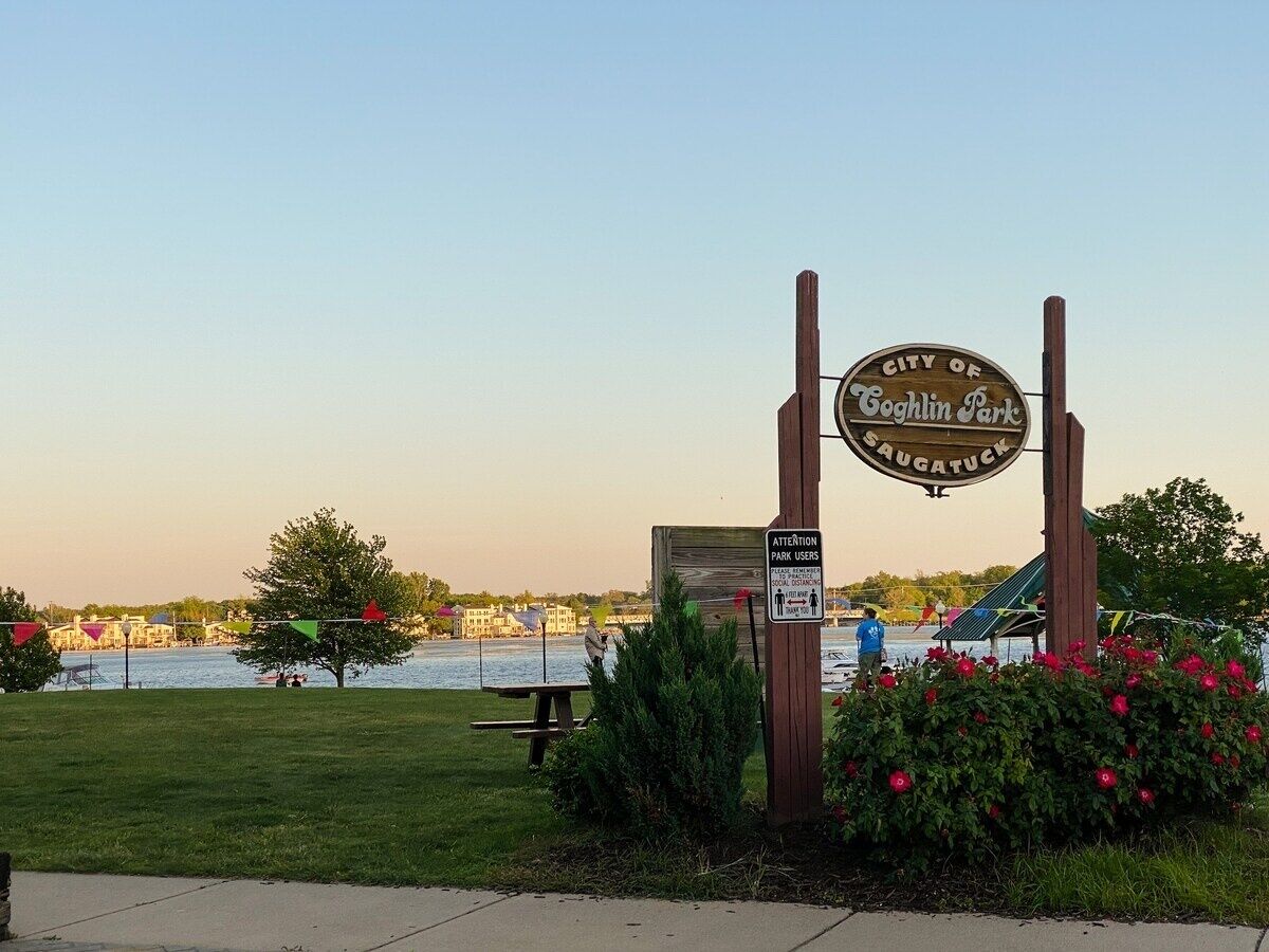 A park entrance sign for the City of Cockeyville Park with a picnic table and a view of the water and buildings in the background.