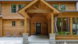 A log cabin with a covered porch, stone steps, and large windows.