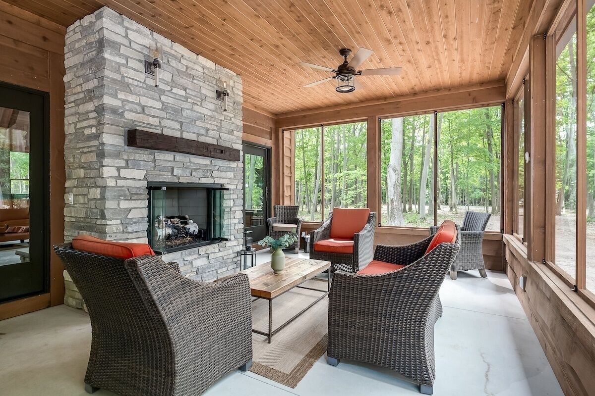 Un interior acogedor con muebles de mimbre, chimenea de piedra y grandes ventanales que dan a un bosque.