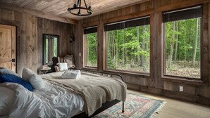 A bedroom with a large bed, wooden walls, and large windows with a forest view.