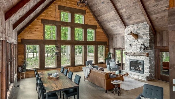 A spacious loft-style room with a large dining table, multiple chairs, a fireplace, and large windows offering a view of the outdoors.