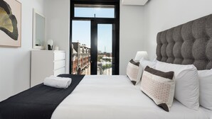 Une chambre d’hôtel moderne, dotée d’un grand lit, offrant une vue sur la ville grâce à une porte vitrée, et présentant une décoration minimaliste.
