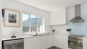 Eine moderne Küche mit weißen Schränken, einem Geschirrspüler von Bosch, einer Edelstahl-Dunstesse und einem Fenster mit Blick auf die Stadt.