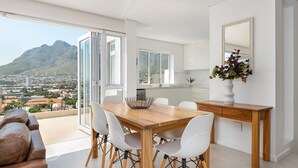 Eine moderne Küche mit einem Holzespeisetisch, weißen Stühlen und Blick auf Stadt und Berge.