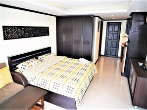 Een moderne slaapkamer met een groot bed, een donkere kast en een bureau met een stoel.