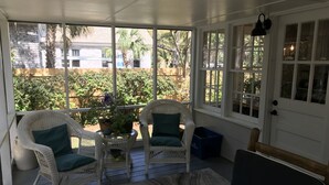 A covered porch with wicker chairs, a small table with a plant, and a view of a garden.