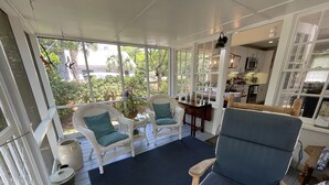 A covered porch with wicker furniture, a dining table, and a kitchen area visible through the open doors.
