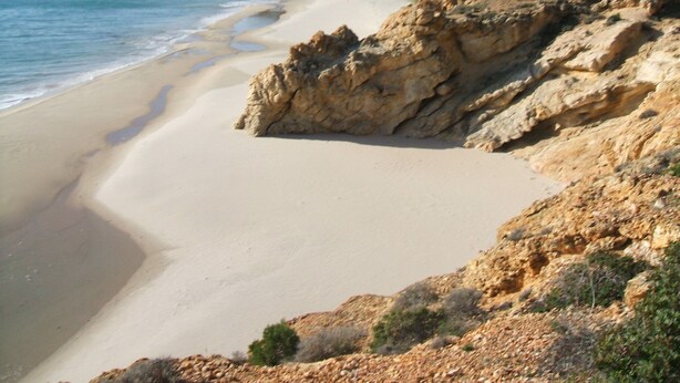 Une plage côtière bordée de falaises rocheuses, offrant une vue dégagée sur la mer.