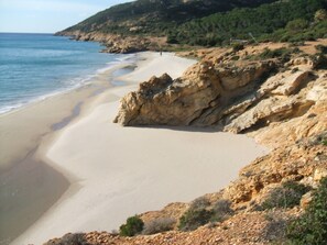 A coastal beach with rocky cliffs and a clear view of the sea.