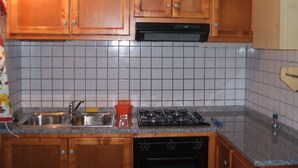 Une cuisine avec des meubles de rangement en bois, une cuisinière à gaz, un évier et un dosseret carrelé.