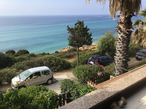A coastal view with a parked car and a white van on a driveway, surrounded by greenery and a stone wall.