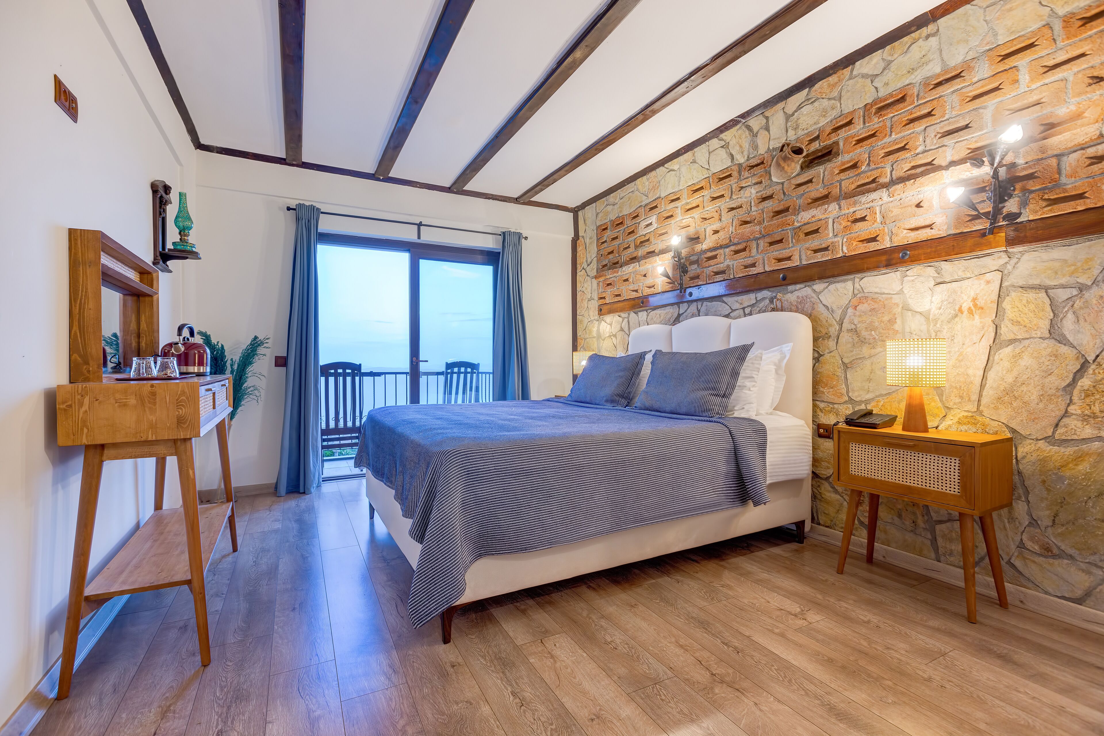 Un dormitorio con una cama, una mesita de noche de madera, un escritorio y una pared de piedra.