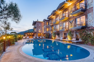 Un área de piscina lujosa con una gran piscina, asientos al aire libre y un edificio de varios pisos con balcones.