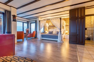 Un dormitorio con cama con dosel, un escritorio rojo y vista al mar.