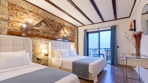 Habitación de hotel con dos camas, una pared de piedra, un balcón y vistas al exterior.
