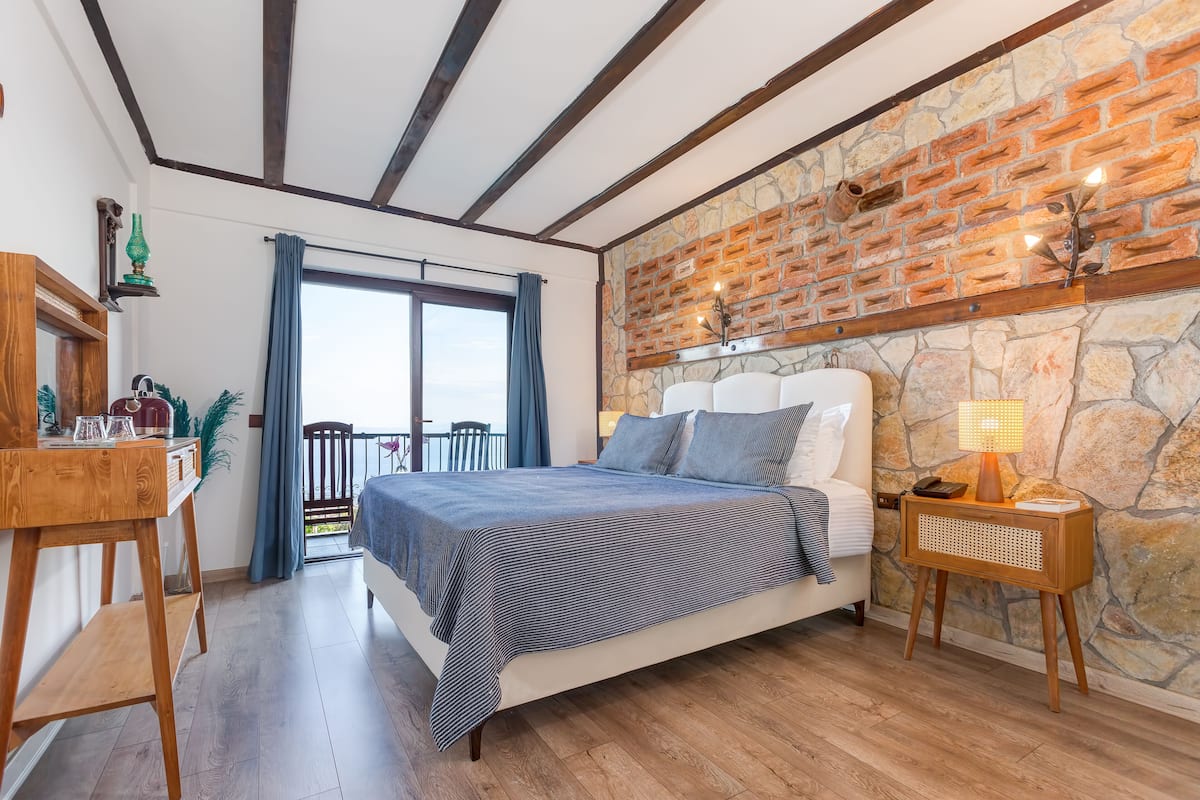 A bedroom with a bed, wooden nightstand, and a stone wall.