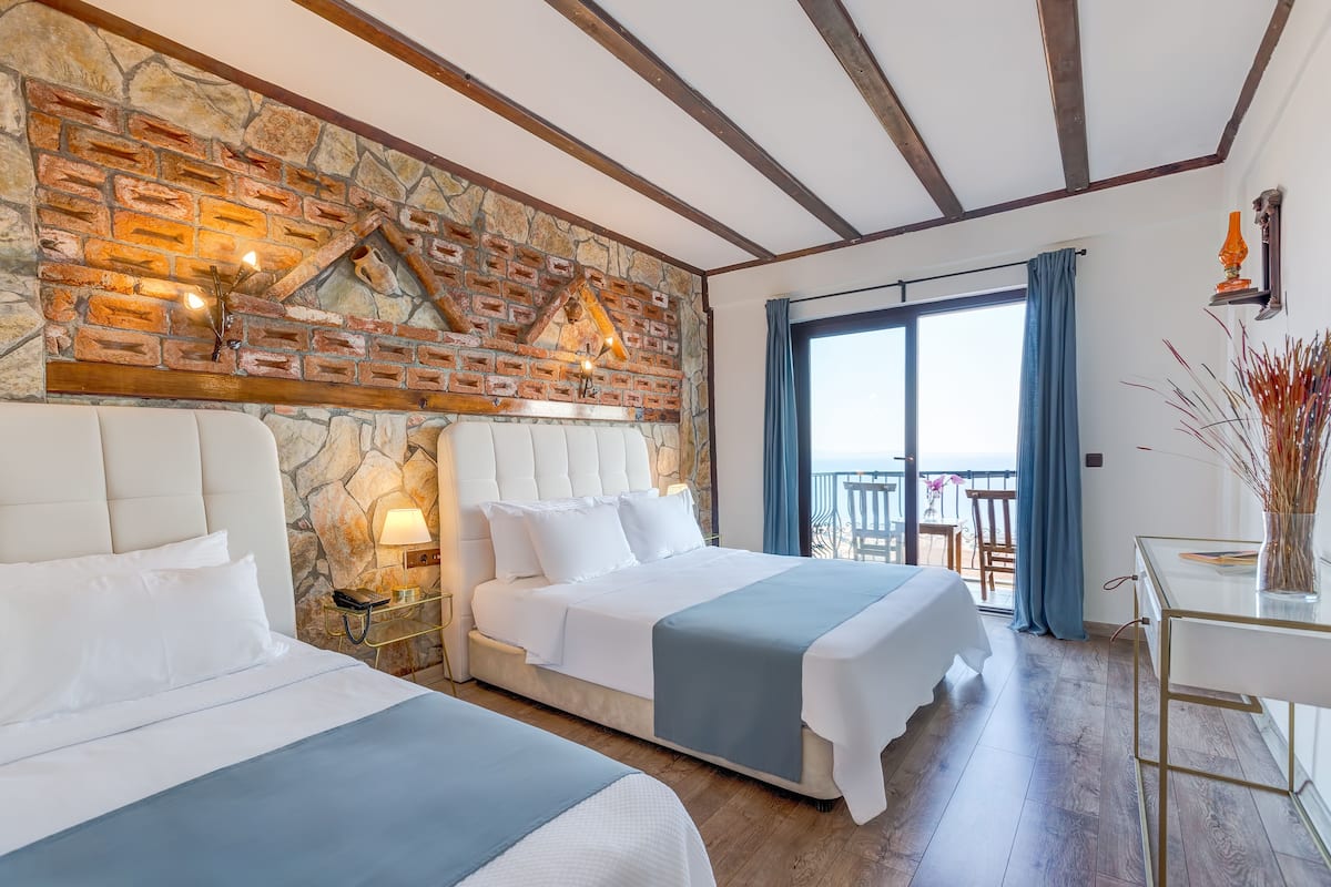 A hotel room with two beds, a stone wall, a balcony with a view, and a modern design.