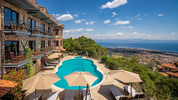 Una piscina con vista al mar, rodeada de sillones y sombrillas.