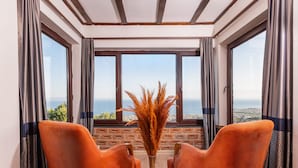 Una habitación con dos sillones naranja, un florero con plumas de miscanthus, y vista al mar a través de amplios ventanales.