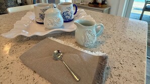 A kitchen counter with a white and blue mug set, a white pitcher, and a spoon on a textured placemat. - SPRAWLING PRIVATE BEACHFRONT - Sleeps 10, perfect for a family, 2 golf carts (Upper Captiva)