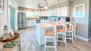 A modern kitchen with white cabinets, a stainless steel refrigerator, a large island with bar stools, and a ceiling fan. - SPRAWLING PRIVATE BEACHFRONT - Sleeps 10, perfect for a family, 2 golf carts (Upper Captiva)