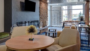 A modern lounge area with a round table, comfortable seating, a stone accent wall, and a large window offering a view of the outside. - Fairfield Inn & Suites by Marriott Grand Rapids Wyoming (Wyoming)