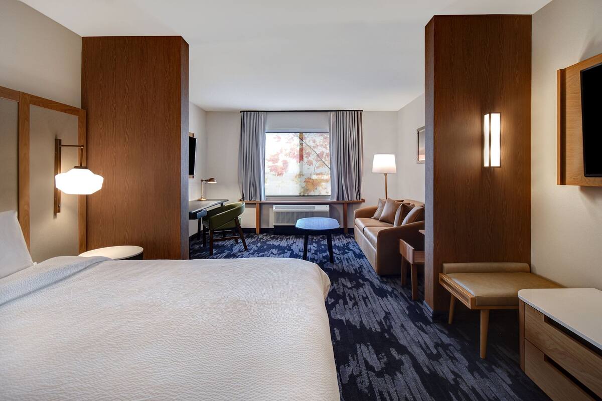 Una habitació d'hotel amb un llit gran, un escriptori, una cadira, una taula petita i un sofà.