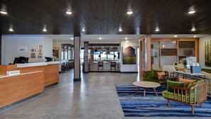 A modern hotel lobby with a reception desk, seating area, and a kitchen in the background. - Fairfield Inn & Suites by Marriott Grand Rapids Wyoming (Wyoming)