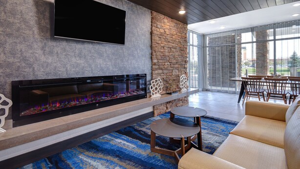 A modern living room with a fireplace, a flat-screen TV mounted on the wall, and a dining area with a table and chairs. - Fairfield Inn & Suites by Marriott Grand Rapids Wyoming (Wyoming)