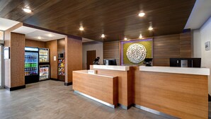A reception area with a wooden reception desk, a vending machine, and a decorative wall piece. - Fairfield Inn & Suites by Marriott Grand Rapids Wyoming (Wyoming)