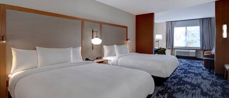 A hotel room with two beds, a desk, a chair, and a large window with curtains.