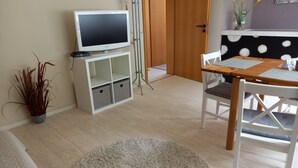 Un soggiorno con televisione a schermo piatto, un tavolo da pranzo con sedie, una pianta in vaso e un tappeto rotondo.