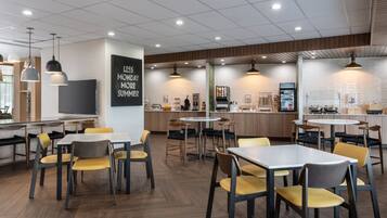 A modern cafe with multiple seating areas, including tables and chairs, and a counter with a menu display.