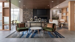 A modern living room with a fireplace, a flat-screen TV, and a round coffee table. - Fairfield Inn & Suites by Marriott Cleveland Tiedeman Road (Brooklyn)