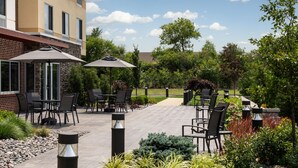 An outdoor patio area with tables and chairs, surrounded by plants and trees. - Fairfield Inn & Suites by Marriott Cleveland Tiedeman Road (Brooklyn)