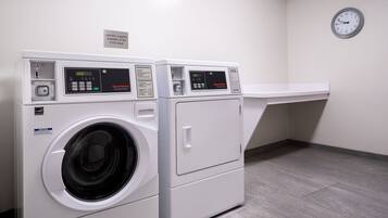 A laundry facility with two front-loading washing machines and a clock on the wall.