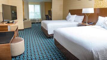 A hotel room with two beds, a desk, a chair, a TV, and a patterned carpet.