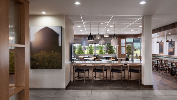 A modern restaurant with a central bar area, multiple seating options, and large windows offering views of greenery. - Fairfield Inn & Suites by Marriott Cleveland Tiedeman Road (Brooklyn)