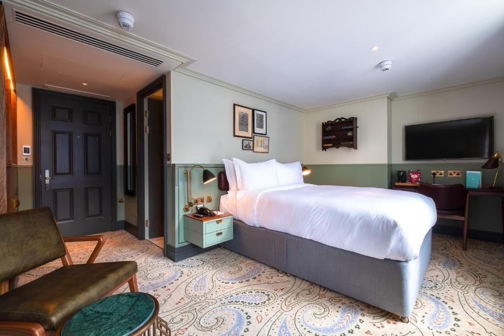 Una habitación de hotel con cama, escritorio, silla, televisor y puerta.