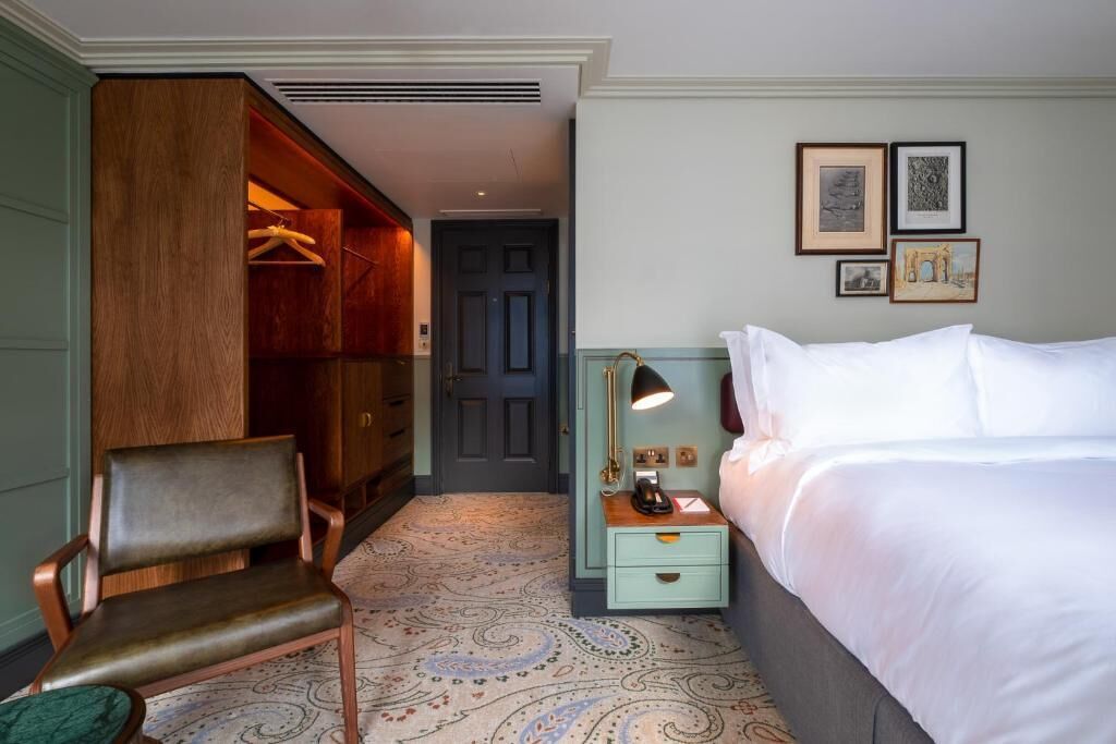 A hotel room with a bed, a chair, a wardrobe, a nightstand, and a door.