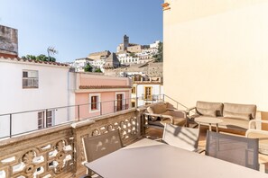 Un balcon agrémenté de mobilier d’extérieur, une vue sur une ville située sur une colline et un bâtiment doté d’une balustrade.