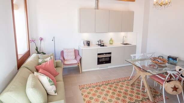 A modern kitchen with white cabinets, a built-in oven, and a glass dining table with chairs.