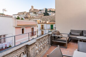 A balcony with outdoor furniture, a view of a hillside town with historic buildings, and a stone balustrade.
