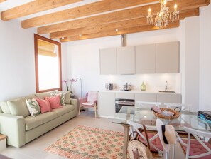 Una sala de estar moderna con un sofá, una mesa de comedor de vidrio y una cocina con armarios y electrodomésticos.