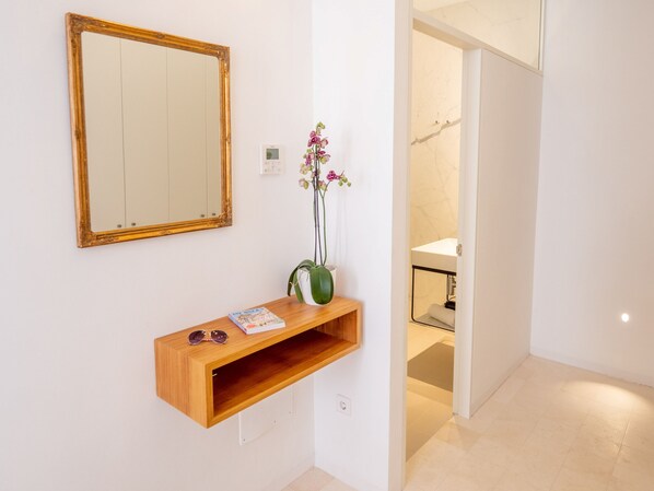 Un pasillo con una consola de madera, un espejo y un florero con flores.