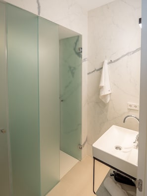 Une salle de bain moderne avec une douche à parois de verre, un mur en marbre et un lavabo blanc avec un miroir.