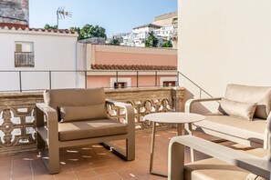 Een terras met twee beige banken en een kleine ronde tafel, omringd door een decoratieve ijzeren hekwerk.