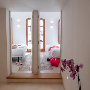 Un couloir menant à deux chambres, avec un plancher en bois, un sac rouge et une orchidée violette.