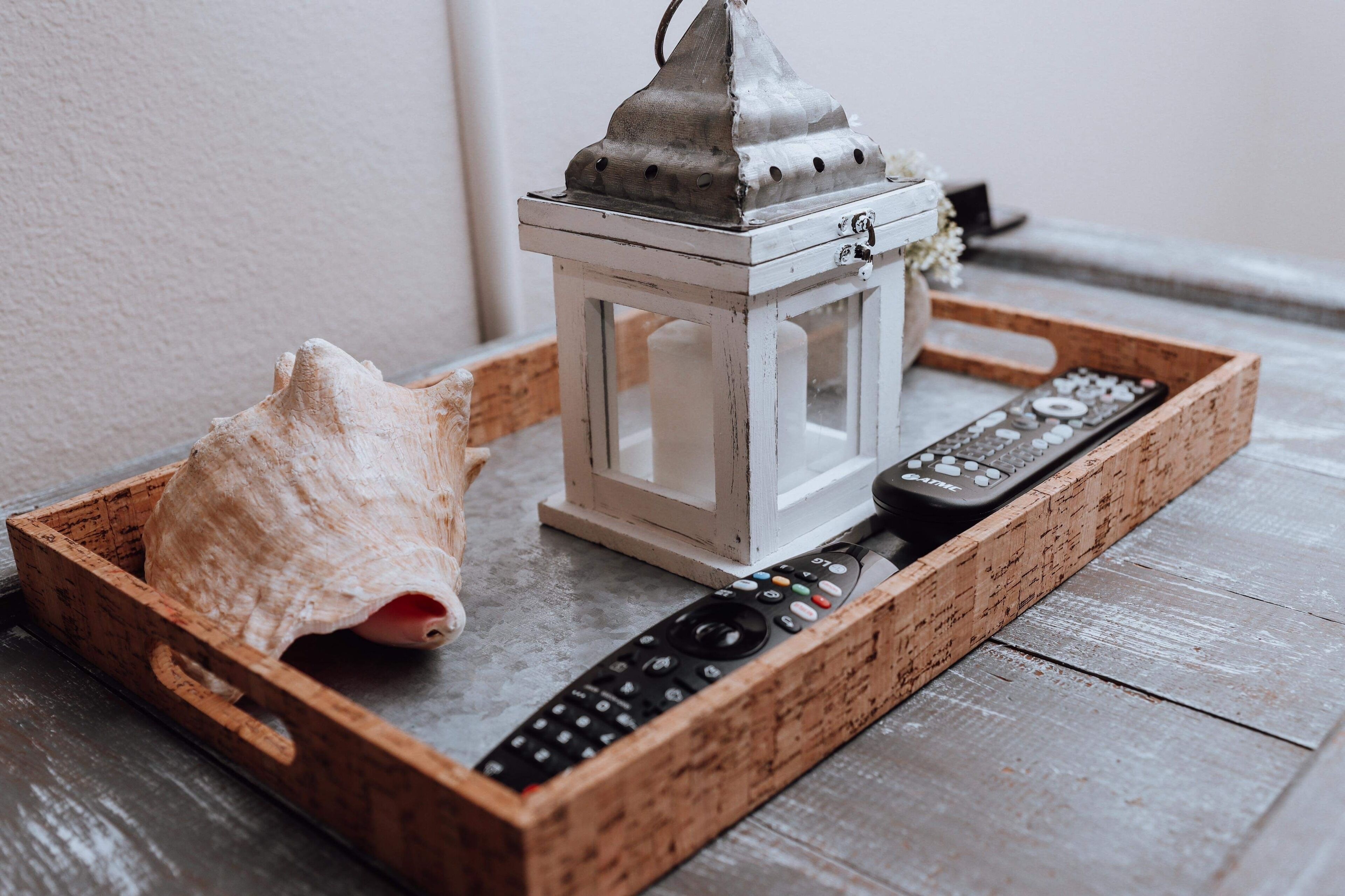 Un plateau en bois avec une lanterne blanche, un coquillage et une télécommande.